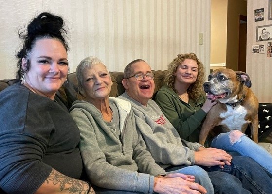 Barry Adams sitting on the couch with three DSPs and his dog. Everyone is smiling.