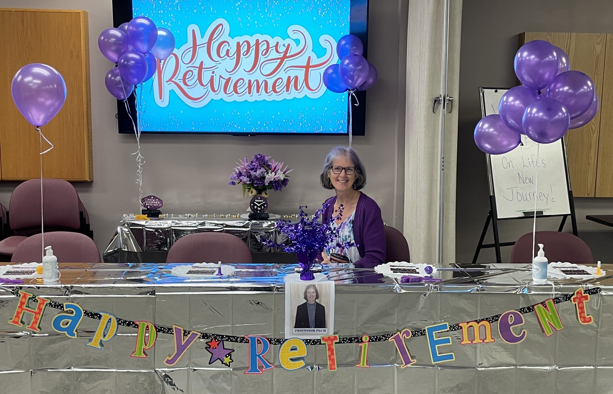 Dr. Angela Ray sitting in front of colorful banner that says Happy Retirement
