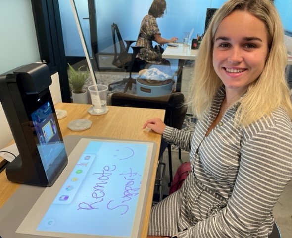 Smiling young woman who works for a remote-support provider sitting at a desk in front of an Amazon device.