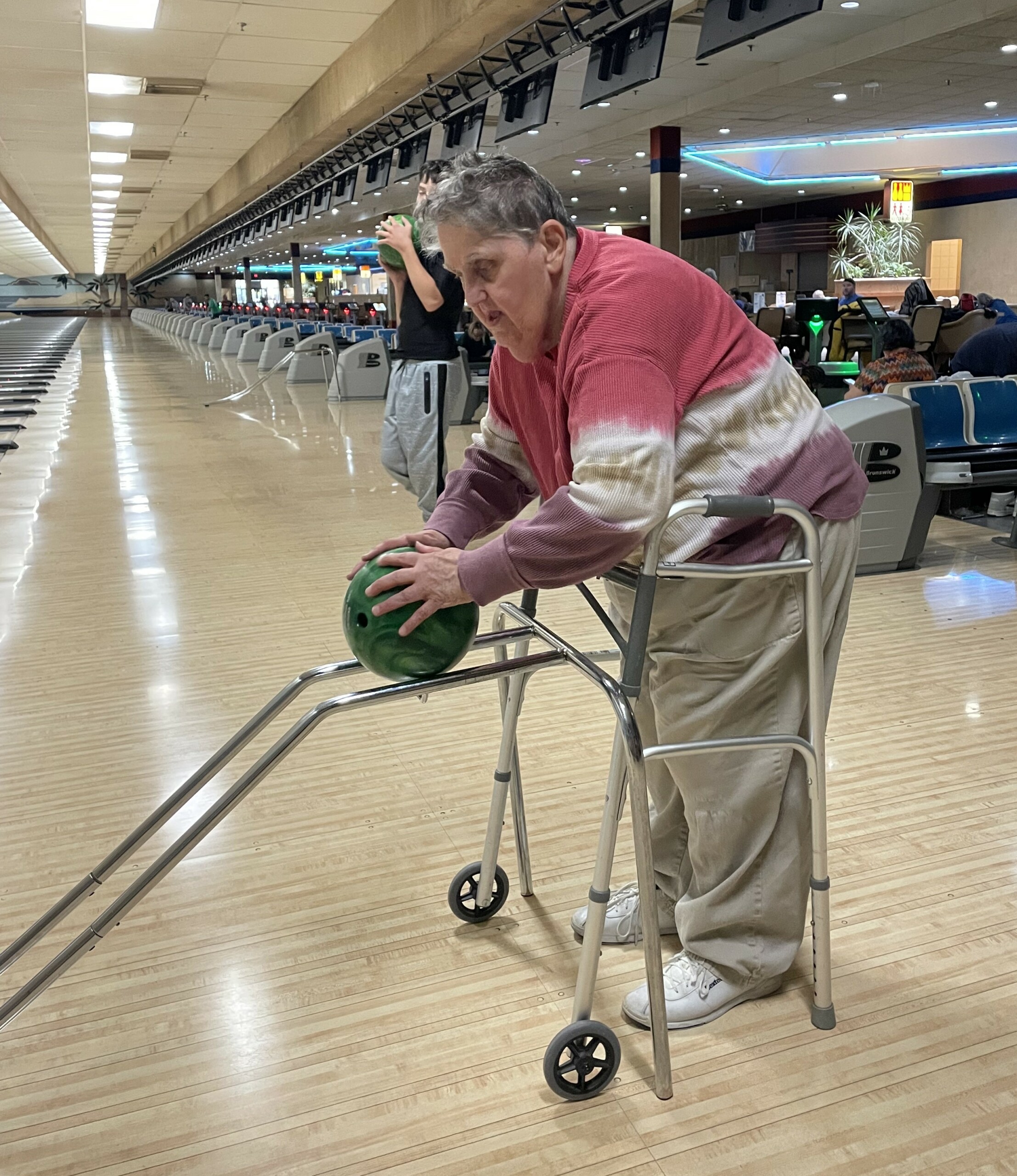 Elderly woman with disabilities using a ball ramp to roll bowling ball down the lane