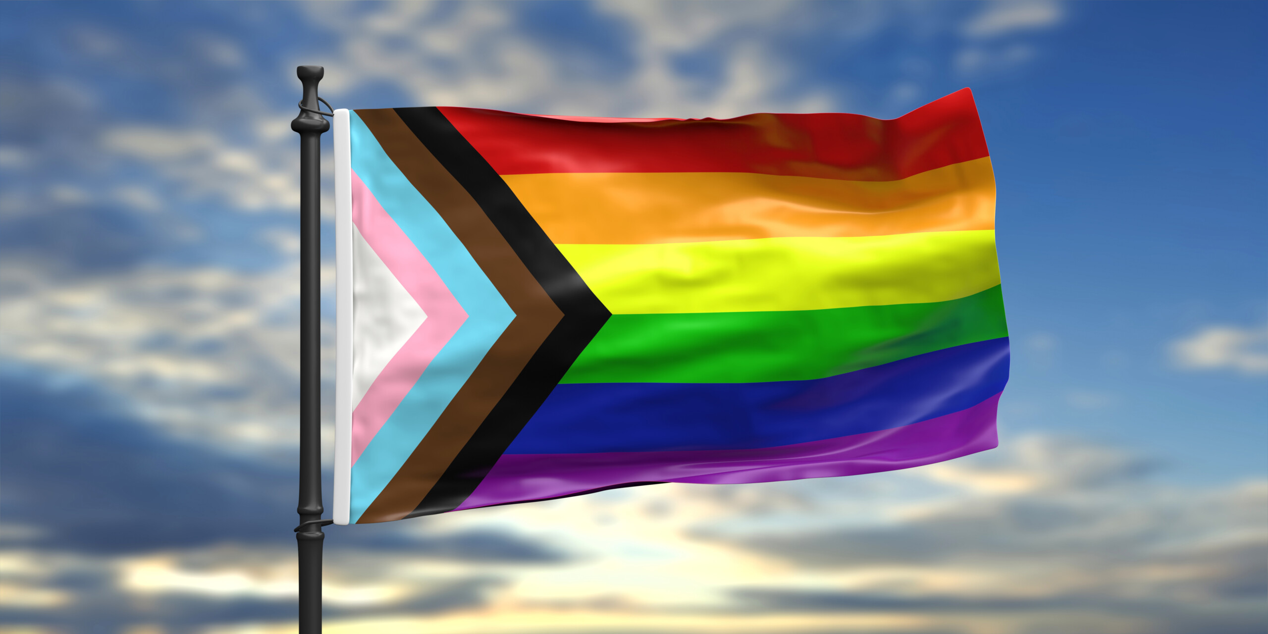 Multi-colored Pride flag flying against a blue sky.